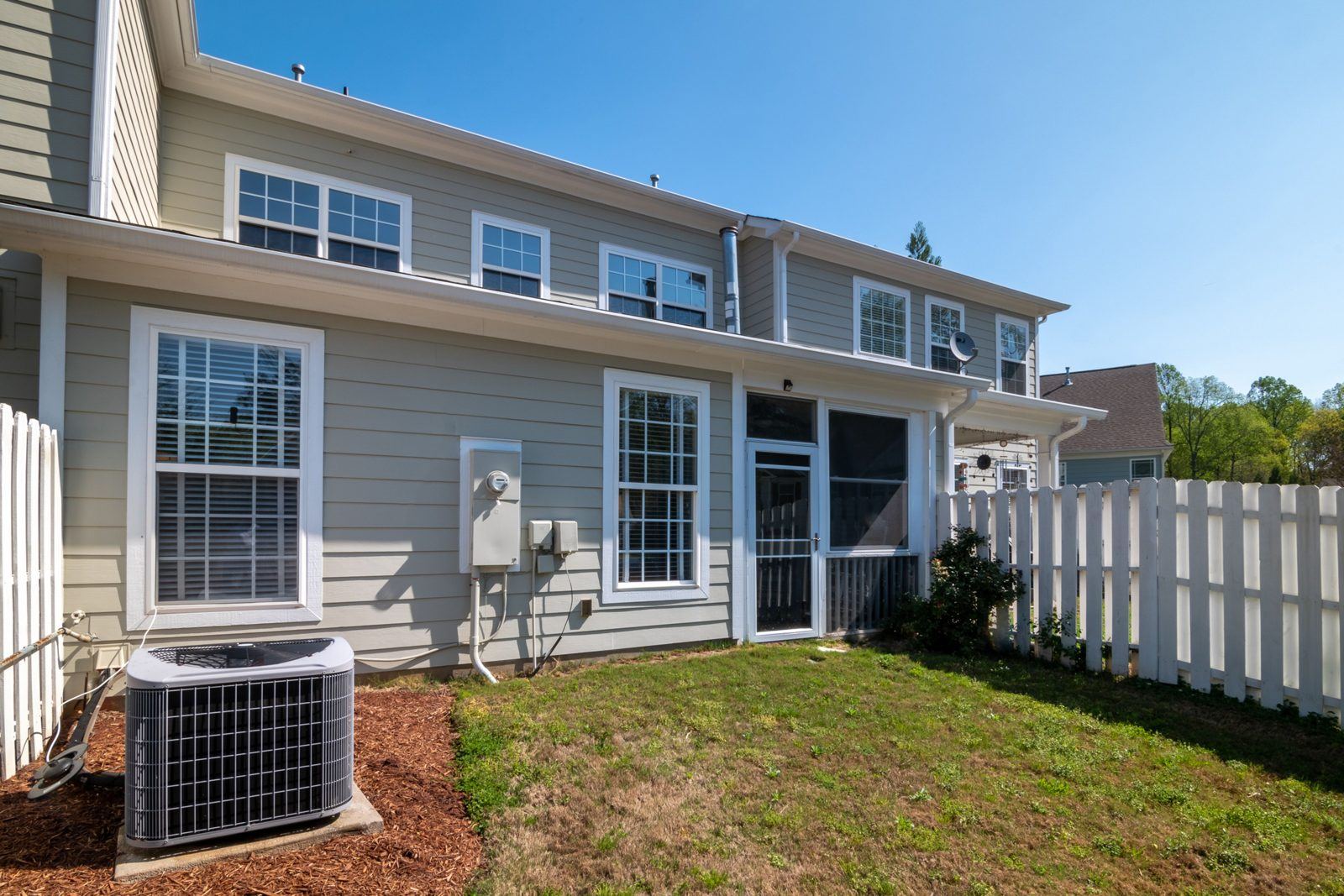 Outdoor air conditioning unit beside a gray house and white fence