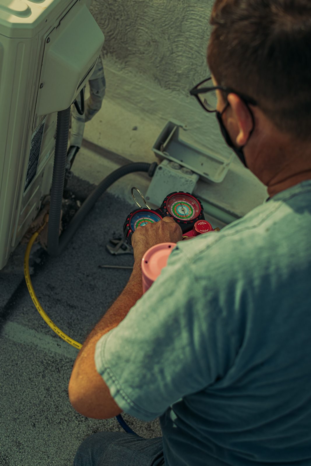 Technician checking an outdoor cooling unit with refrigerant gauges
