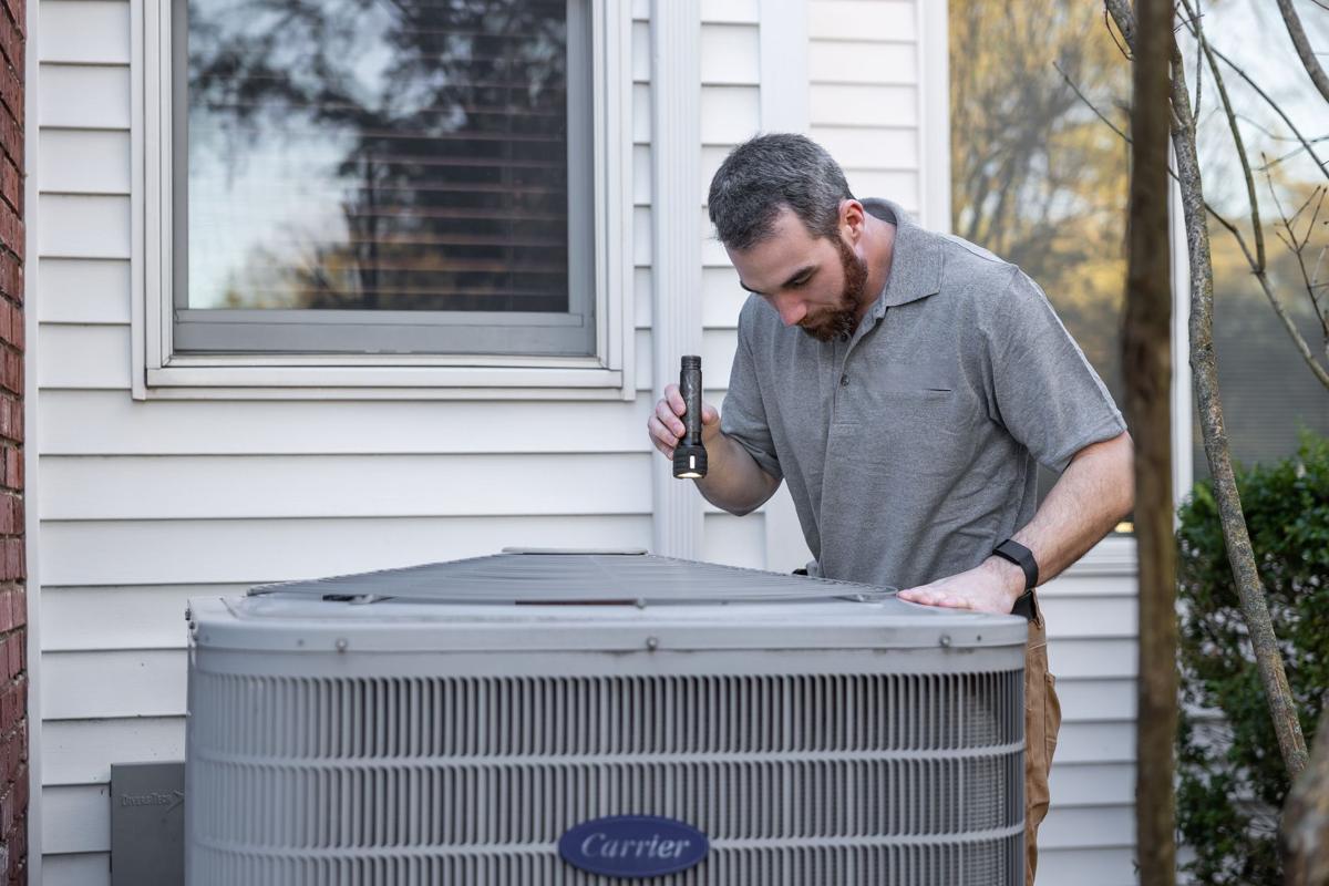 Technician repairing an outdoor air conditioner beside a home